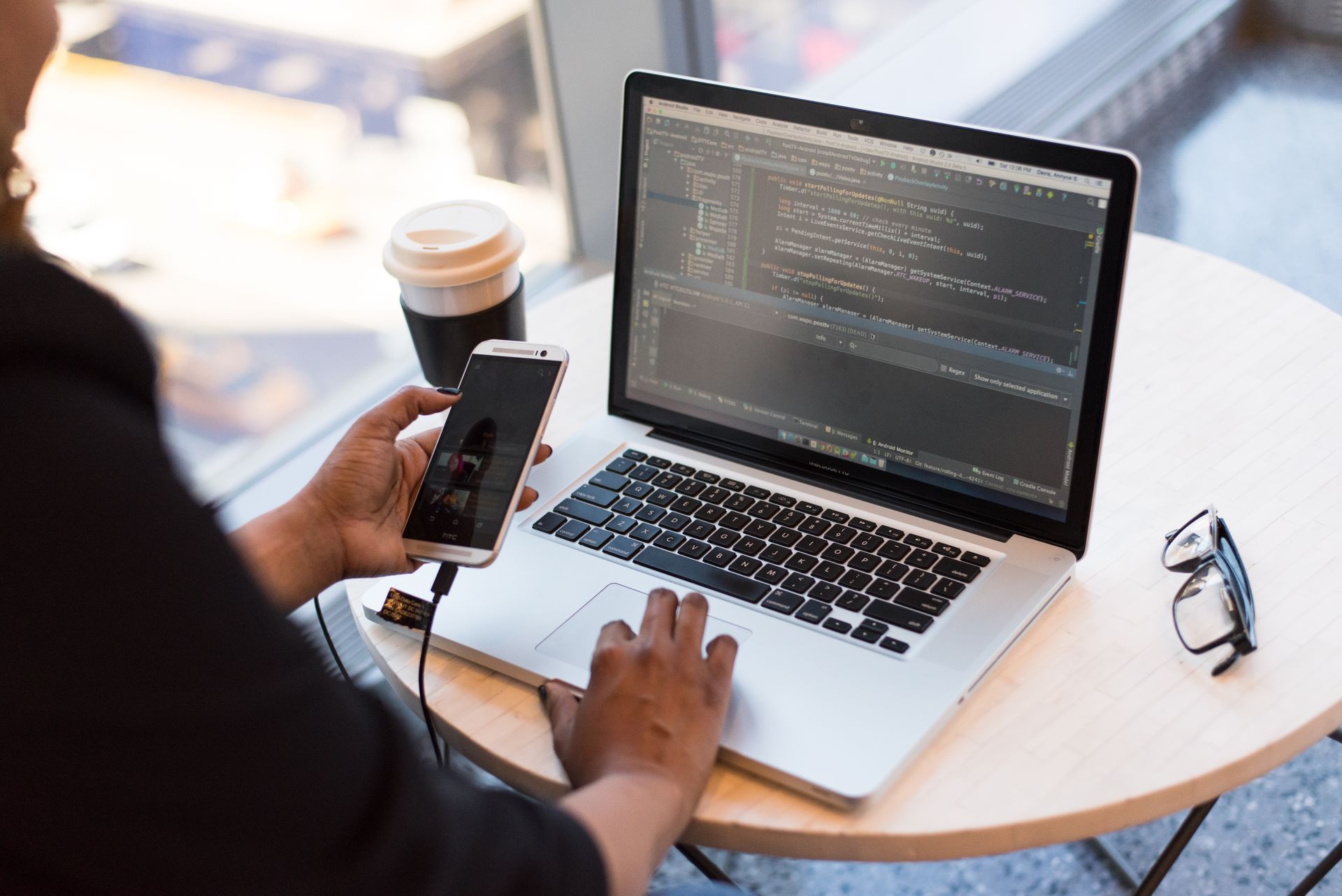 A developer holding a phone while editing code on a laptop, the setup used to compare fold poses with Xcode on a Mac
